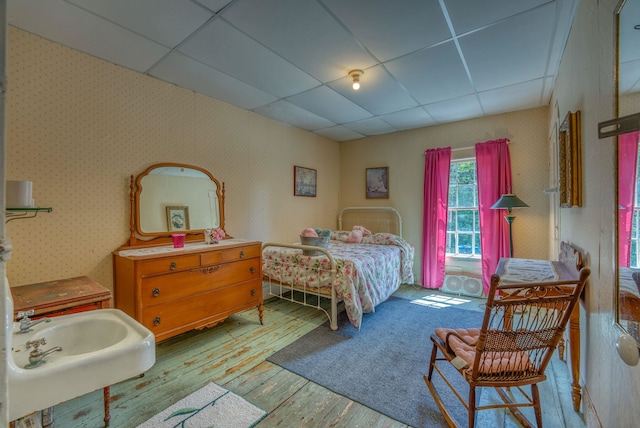 bedroom with wallpapered walls, a drop ceiling, and wood finished floors