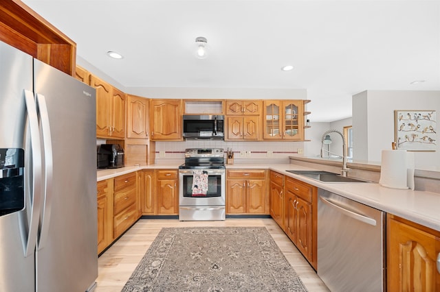 kitchen featuring stainless steel appliances, tasteful backsplash, light countertops, light wood-style flooring, and a sink