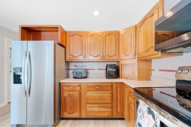 kitchen featuring stainless steel appliances, backsplash, light countertops, and light wood-style floors