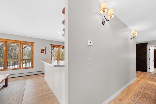 corridor with light wood-style floors, a baseboard radiator, and baseboards