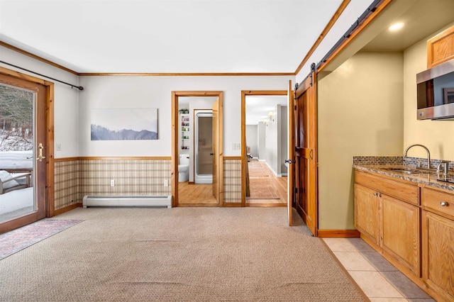 interior space featuring a barn door, a baseboard radiator, light colored carpet, a wainscoted wall, and a sink