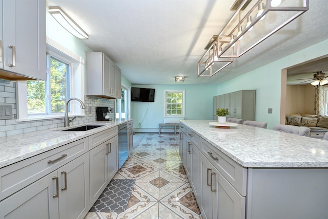 kitchen featuring backsplash, stainless steel dishwasher, a kitchen island, a sink, and plenty of natural light