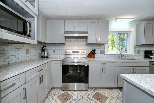 kitchen with appliances with stainless steel finishes, a sink, gray cabinetry, under cabinet range hood, and backsplash