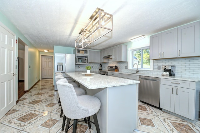 kitchen featuring a breakfast bar area, under cabinet range hood, gray cabinetry, a sink, and appliances with stainless steel finishes