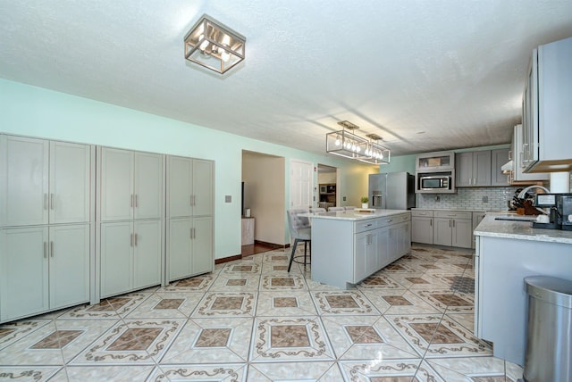 kitchen featuring gray cabinetry, stainless steel appliances, a sink, light countertops, and decorative backsplash