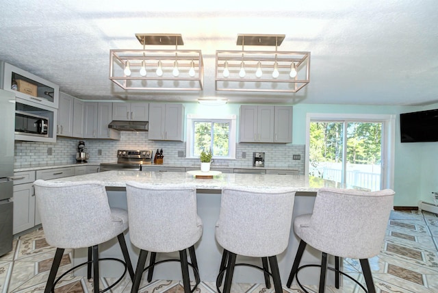 kitchen featuring under cabinet range hood, tasteful backsplash, appliances with stainless steel finishes, and gray cabinetry