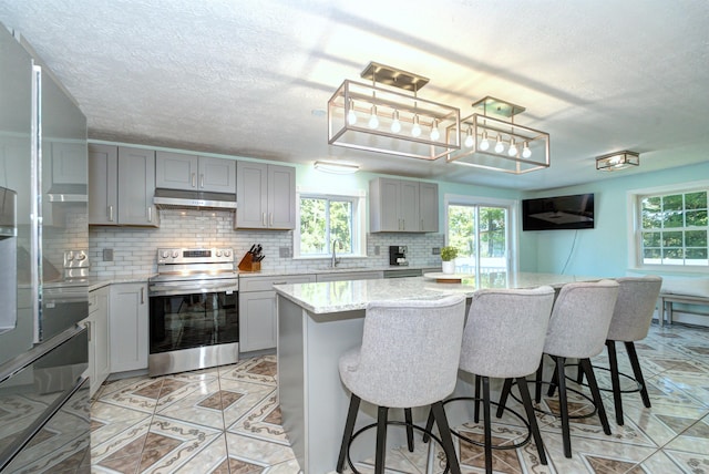 kitchen featuring tasteful backsplash, stainless steel electric stove, gray cabinetry, under cabinet range hood, and a sink