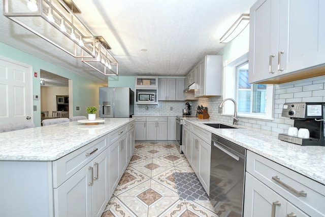 kitchen with light stone counters, stainless steel appliances, a sink, backsplash, and a center island