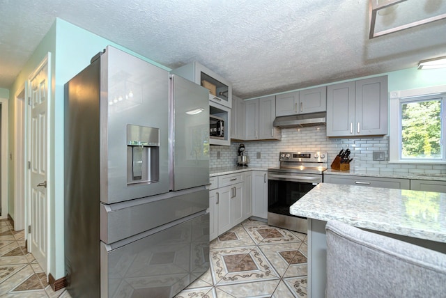 kitchen featuring light tile patterned floors, under cabinet range hood, stainless steel appliances, gray cabinets, and backsplash