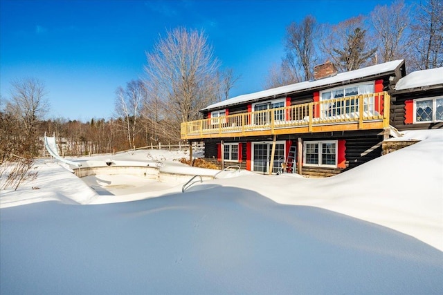 snow covered house featuring a chimney, log siding, and a wooden deck