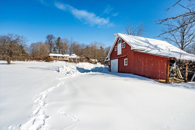 yard layered in snow featuring a garage, an outbuilding, and a barn