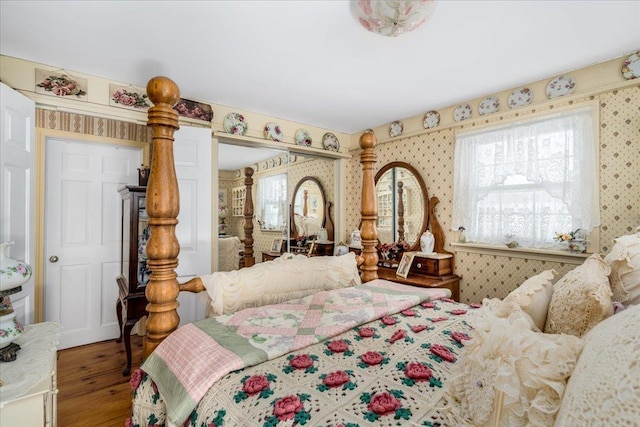 bedroom with wallpapered walls, a closet, multiple windows, and wood finished floors