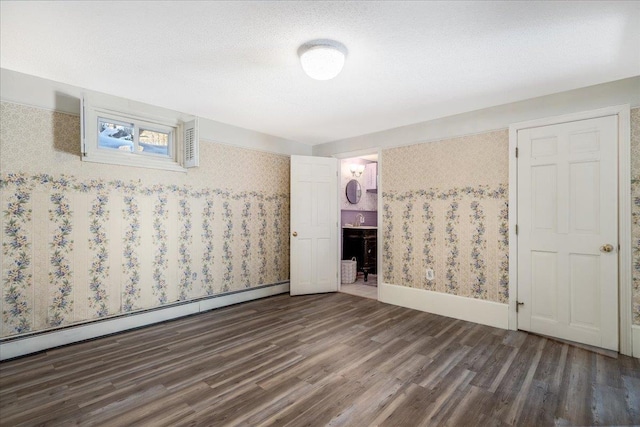 empty room with baseboards, wood finished floors, baseboard heating, a textured ceiling, and a sink