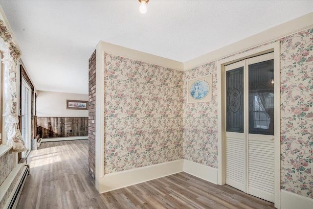 spare room featuring a baseboard radiator, a baseboard heating unit, wood finished floors, baseboards, and wallpapered walls