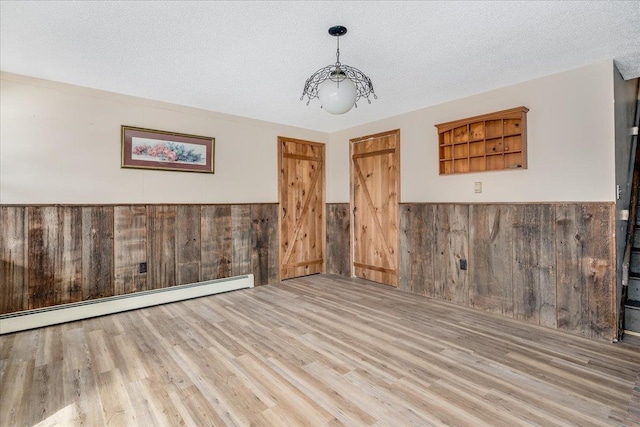 empty room with a wainscoted wall, wood walls, a textured ceiling, and wood finished floors