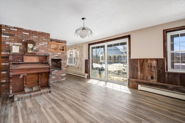 living room with a textured ceiling, baseboard heating, wood finished floors, and a wainscoted wall