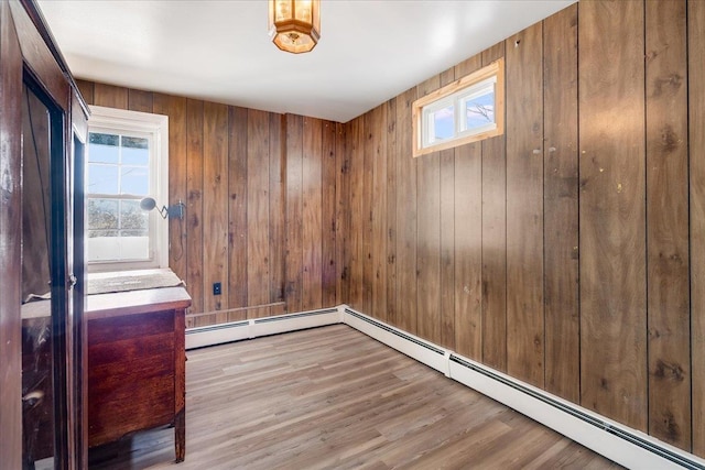 empty room with wood walls, a baseboard radiator, and wood finished floors