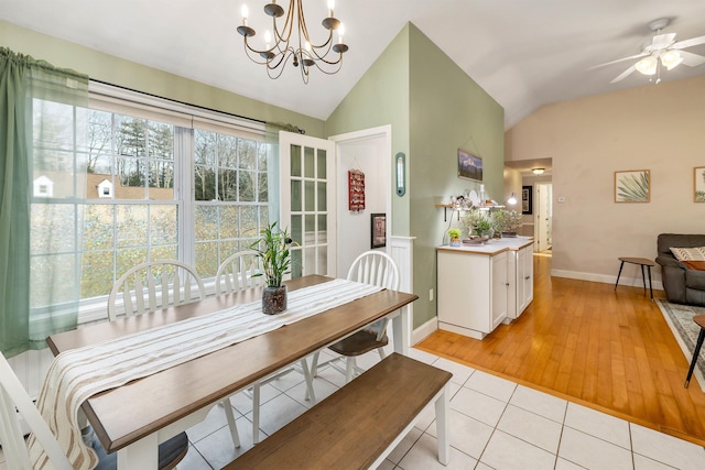 dining space with ceiling fan with notable chandelier, vaulted ceiling, baseboards, and light tile patterned floors