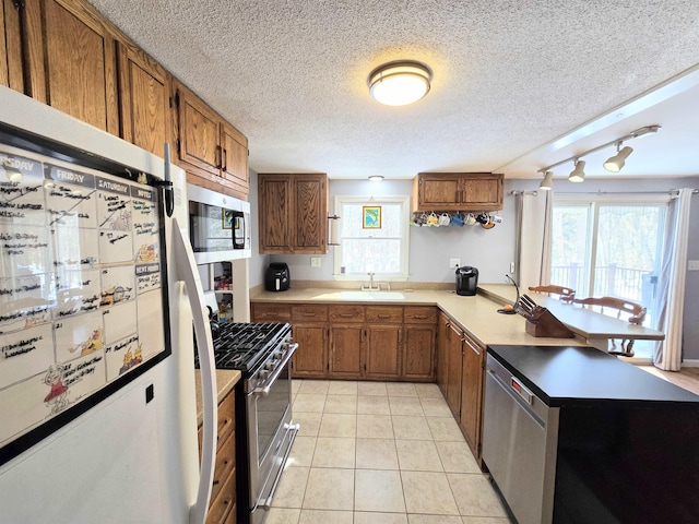 kitchen with light tile patterned floors, appliances with stainless steel finishes, brown cabinetry, and a sink