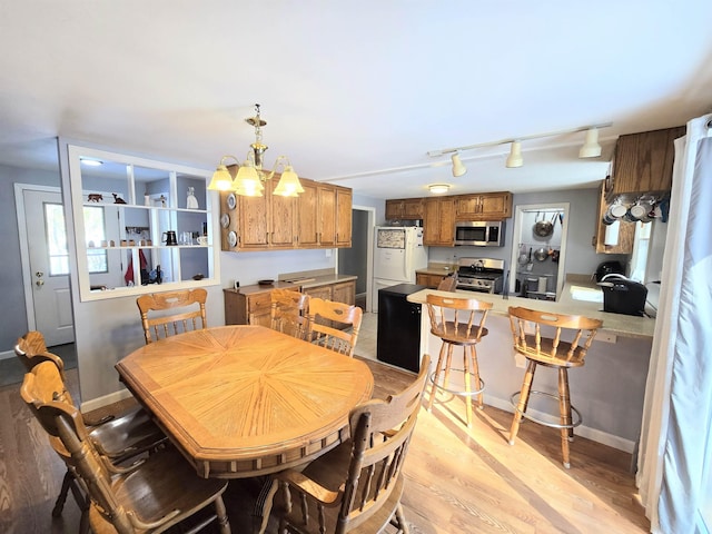 dining space with baseboards, track lighting, light wood-type flooring, and a notable chandelier