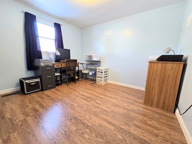 office space with visible vents, a textured ceiling, baseboards, and wood finished floors