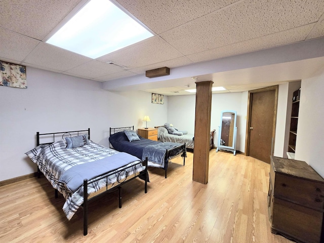 bedroom featuring visible vents, a drop ceiling, light wood-style flooring, and baseboards