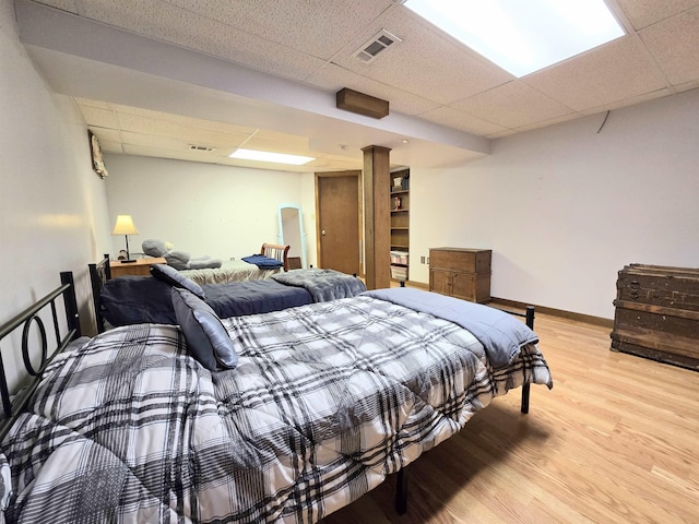 bedroom with a paneled ceiling, light wood-type flooring, visible vents, and baseboards