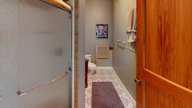 bathroom featuring toilet, baseboards, a shower with door, and tile patterned floors