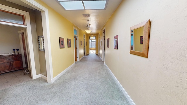 hallway with a skylight, baseboards, and light colored carpet