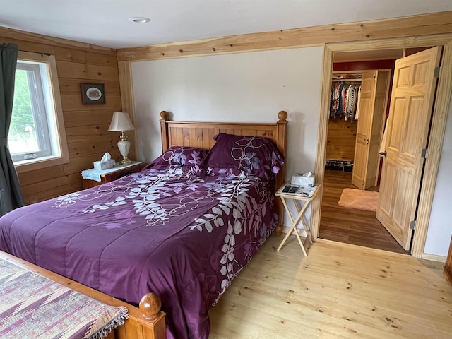 bedroom with a spacious closet, a closet, wood finished floors, and wooden walls