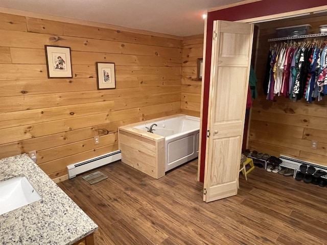 bathroom featuring a baseboard heating unit, wood walls, vanity, wood finished floors, and a bath