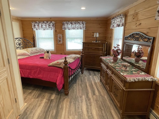 bedroom with wood walls, multiple windows, a baseboard heating unit, and wood finished floors