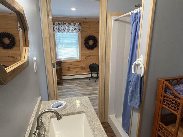 bathroom featuring a stall shower, a baseboard radiator, wooden walls, and a sink