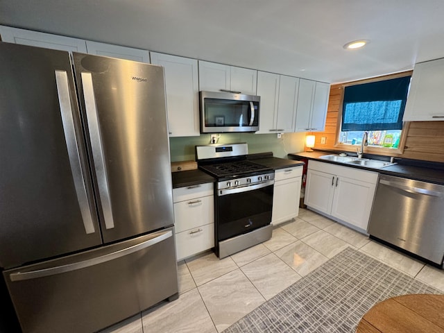 kitchen featuring dark countertops, white cabinets, stainless steel appliances, and a sink