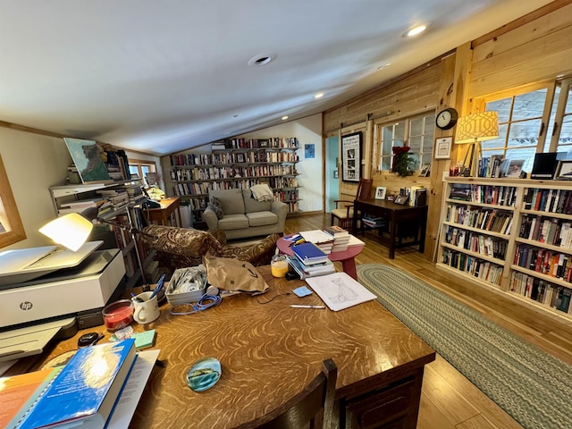 interior space featuring lofted ceiling, wall of books, and wood finished floors