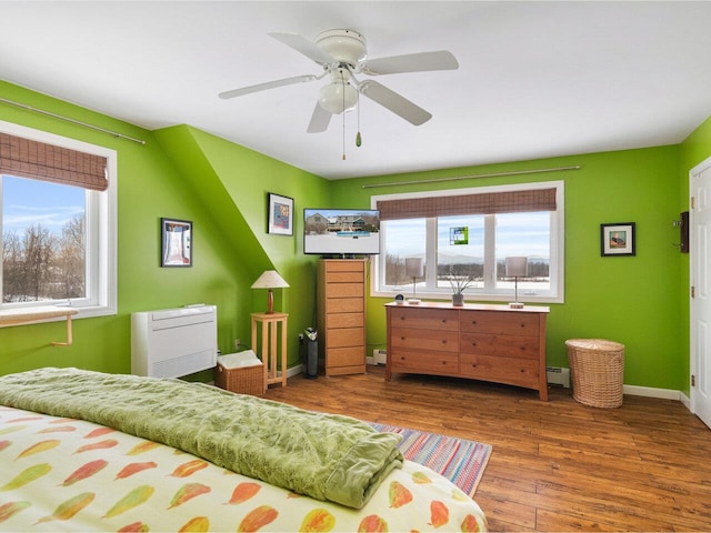 bedroom with multiple windows, baseboards, baseboard heating, and wood finished floors