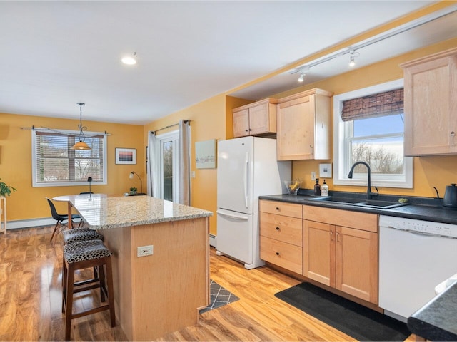 kitchen with white appliances, light brown cabinets, a kitchen island, and a sink