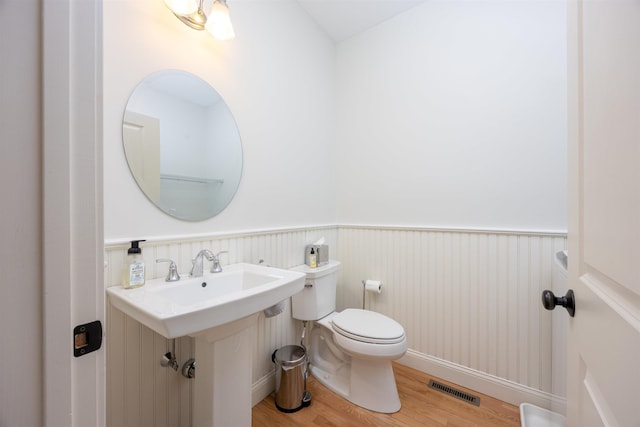 half bathroom with a wainscoted wall, visible vents, toilet, and wood finished floors