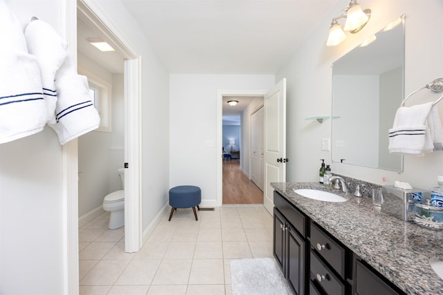 ensuite bathroom with double vanity, toilet, a sink, tile patterned flooring, and baseboards