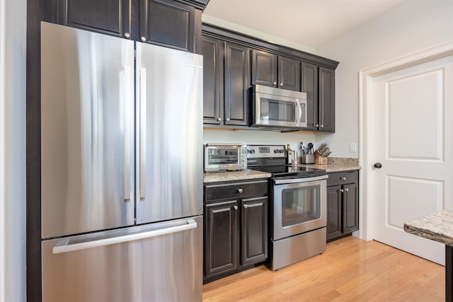 kitchen with a toaster, appliances with stainless steel finishes, light stone countertops, and light wood-style floors