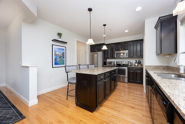 kitchen featuring a breakfast bar, a sink, appliances with stainless steel finishes, light wood-type flooring, and a center island