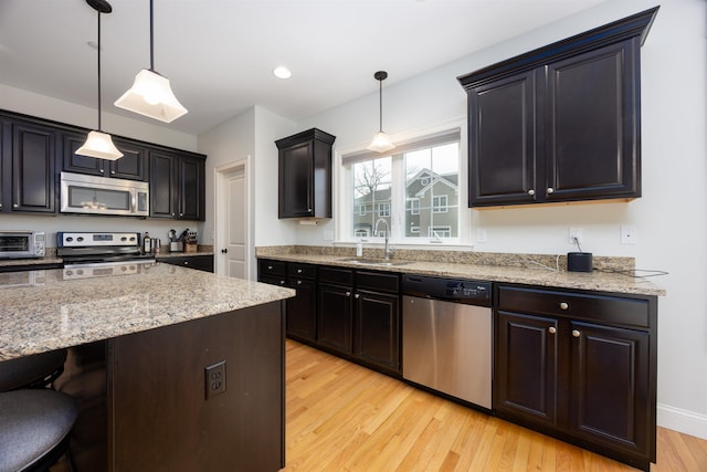 kitchen featuring a toaster, light wood finished floors, stainless steel appliances, a sink, and a kitchen breakfast bar