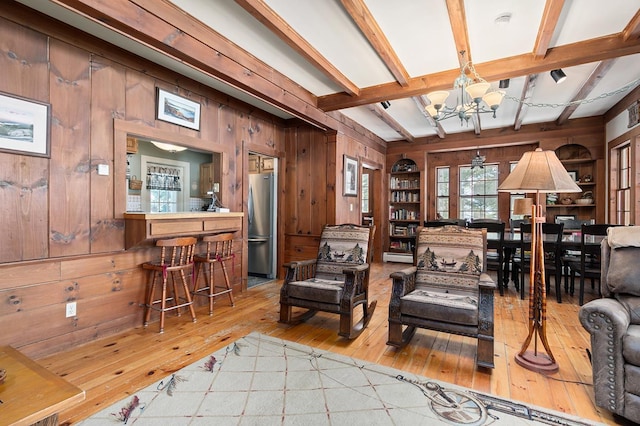 living area featuring light wood-type flooring, wood walls, a chandelier, and beam ceiling