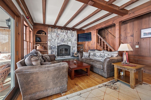 living area with beam ceiling, stairway, a stone fireplace, wooden walls, and hardwood / wood-style flooring