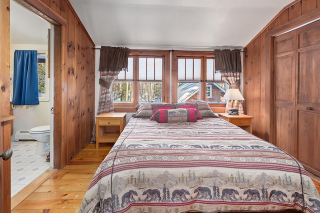 bedroom with light wood-type flooring, connected bathroom, wooden walls, and baseboard heating