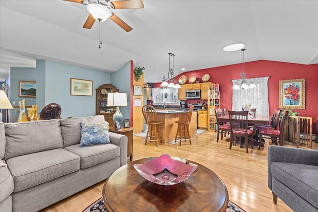 living area with lofted ceiling, light wood finished floors, and ceiling fan with notable chandelier