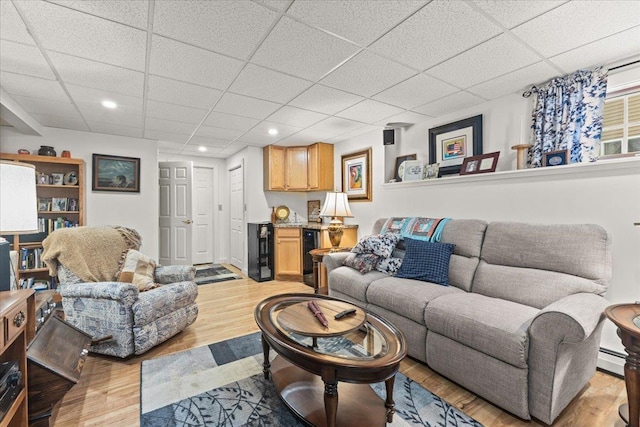 living area featuring wine cooler, a paneled ceiling, recessed lighting, light wood-style floors, and a dry bar