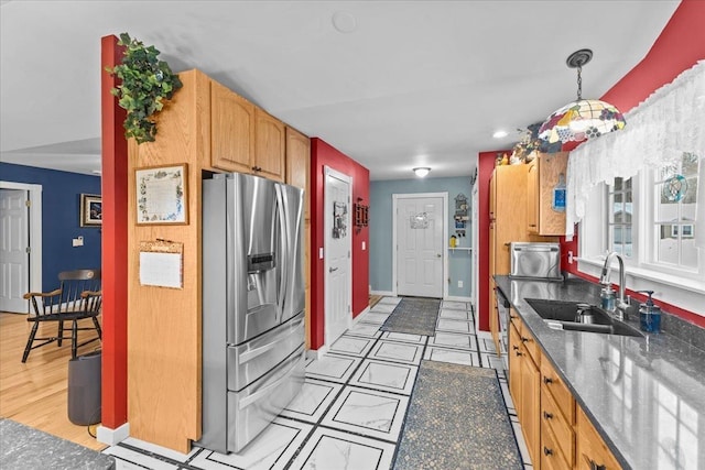 kitchen with a sink, baseboards, stainless steel refrigerator with ice dispenser, dark stone counters, and pendant lighting