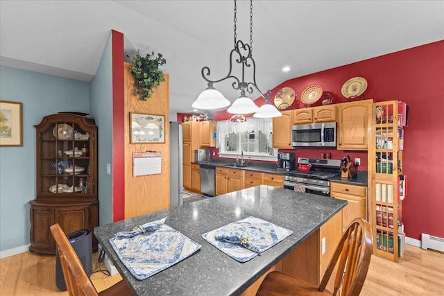 kitchen with light wood finished floors, dark countertops, vaulted ceiling, stainless steel appliances, and a sink