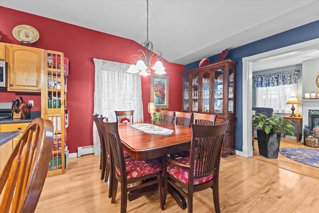 dining room with a baseboard radiator, light wood-style flooring, vaulted ceiling, a fireplace, and a chandelier